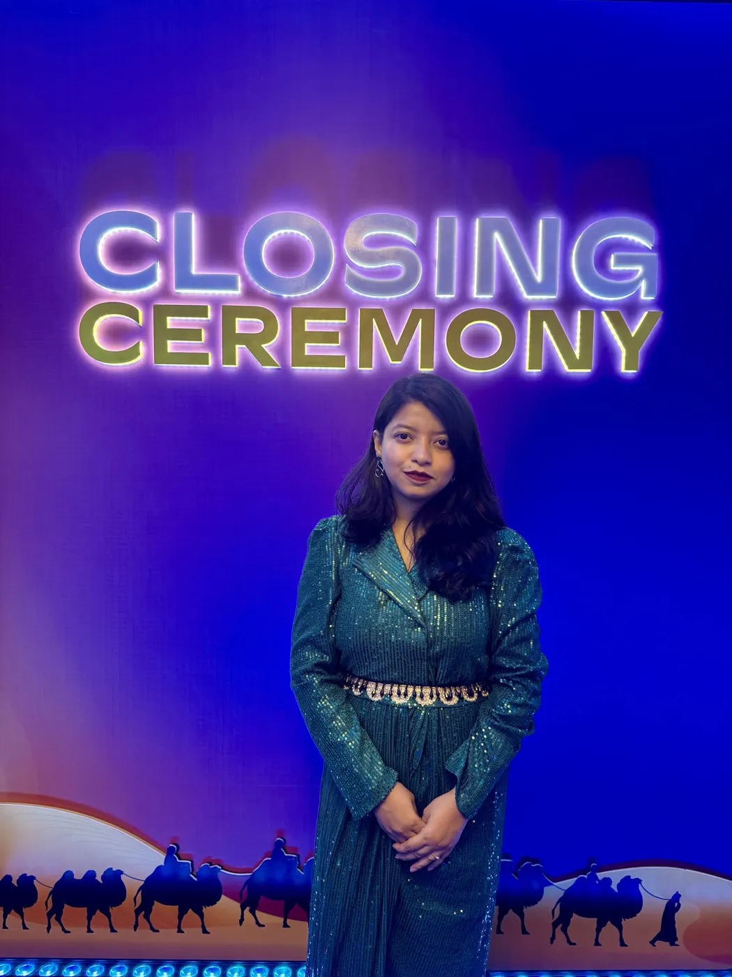 Afshana in a green sequin dress in front of the ASPAC closing ceremony sign