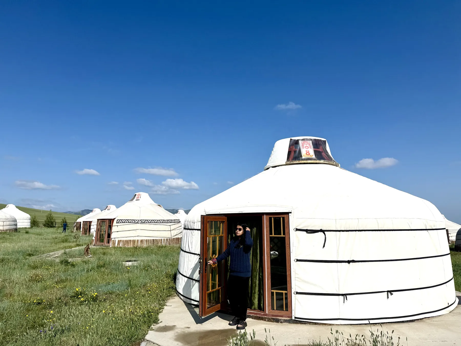 Afshana opening the door of a white ger at a ger camp under a deep blue sky