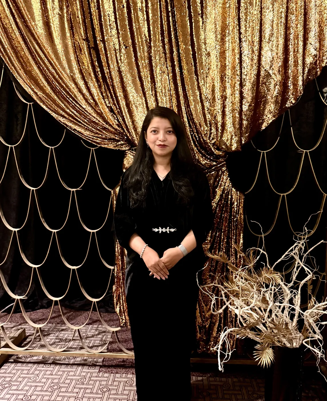 Afshana in black in front of a gold curtain