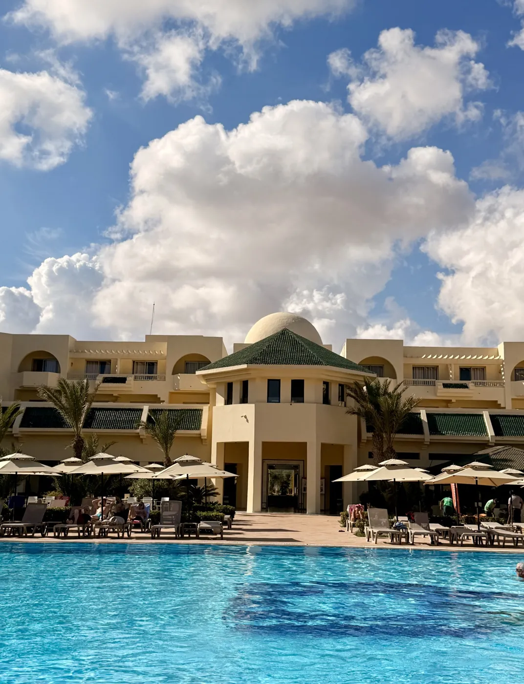 A pool and white domed buildings under a cloudy sky in Djerba