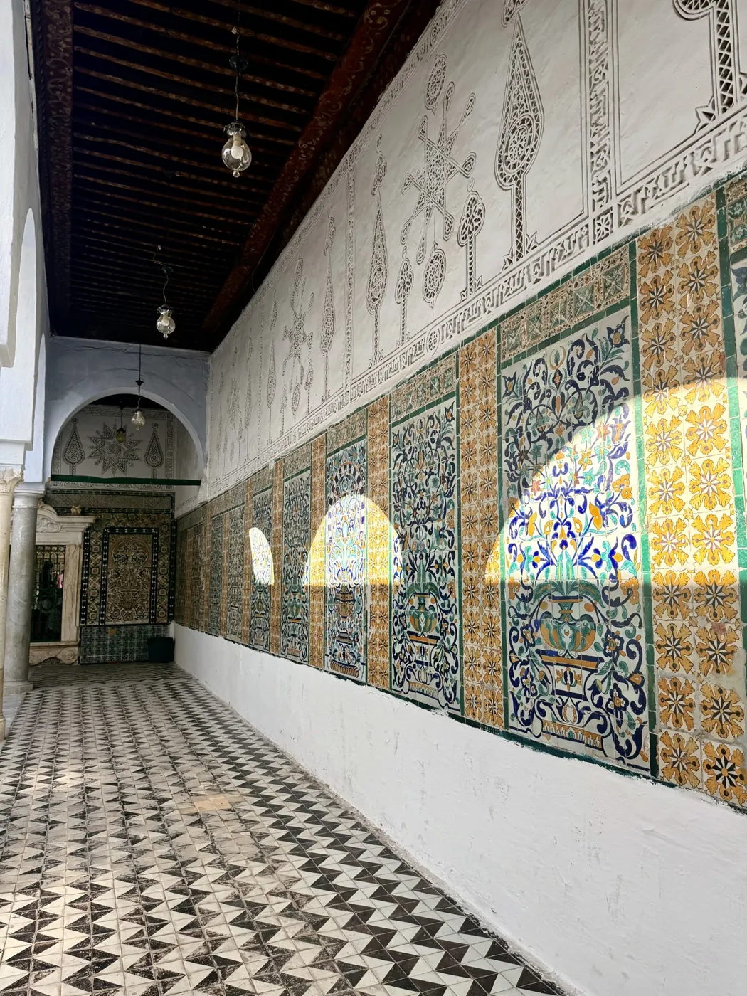 A long corridor lined with painted tiles and carved stucco in Kairouan