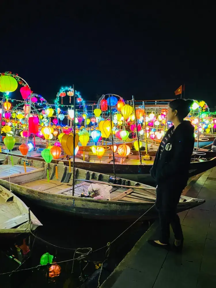 Afshana standing beside boats covered in glowing lanterns in Hoi An