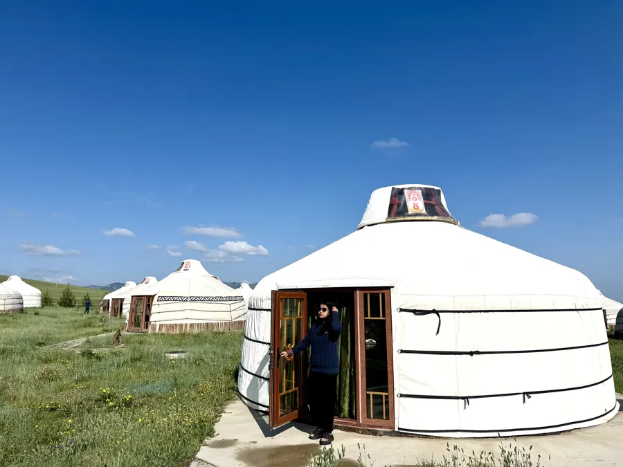 Afshana Diya opening the door of a white ger at a ger camp under a deep blue sky