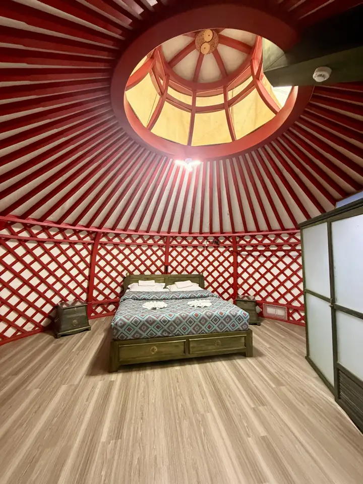 Inside a ger: red lattice walls, a wooden bed and a round skylight